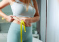 Fatty young woman hand holding excessive belly fat with measure tape, woman diet lifestyle